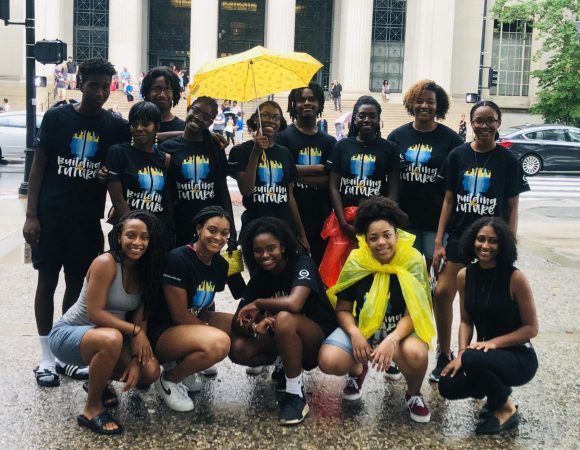 REEX program high school students of color posing in the rain in front of 77 Massachusetts Ave.