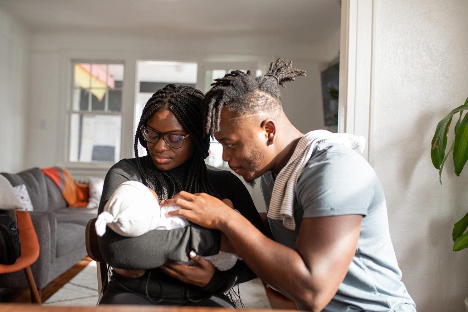 African American parents coo at their newborn swaddled in a blanket