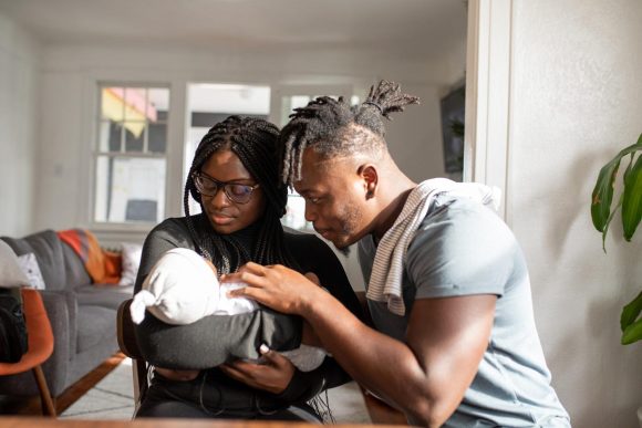 African American parents coo at their newborn swaddled in a blanket