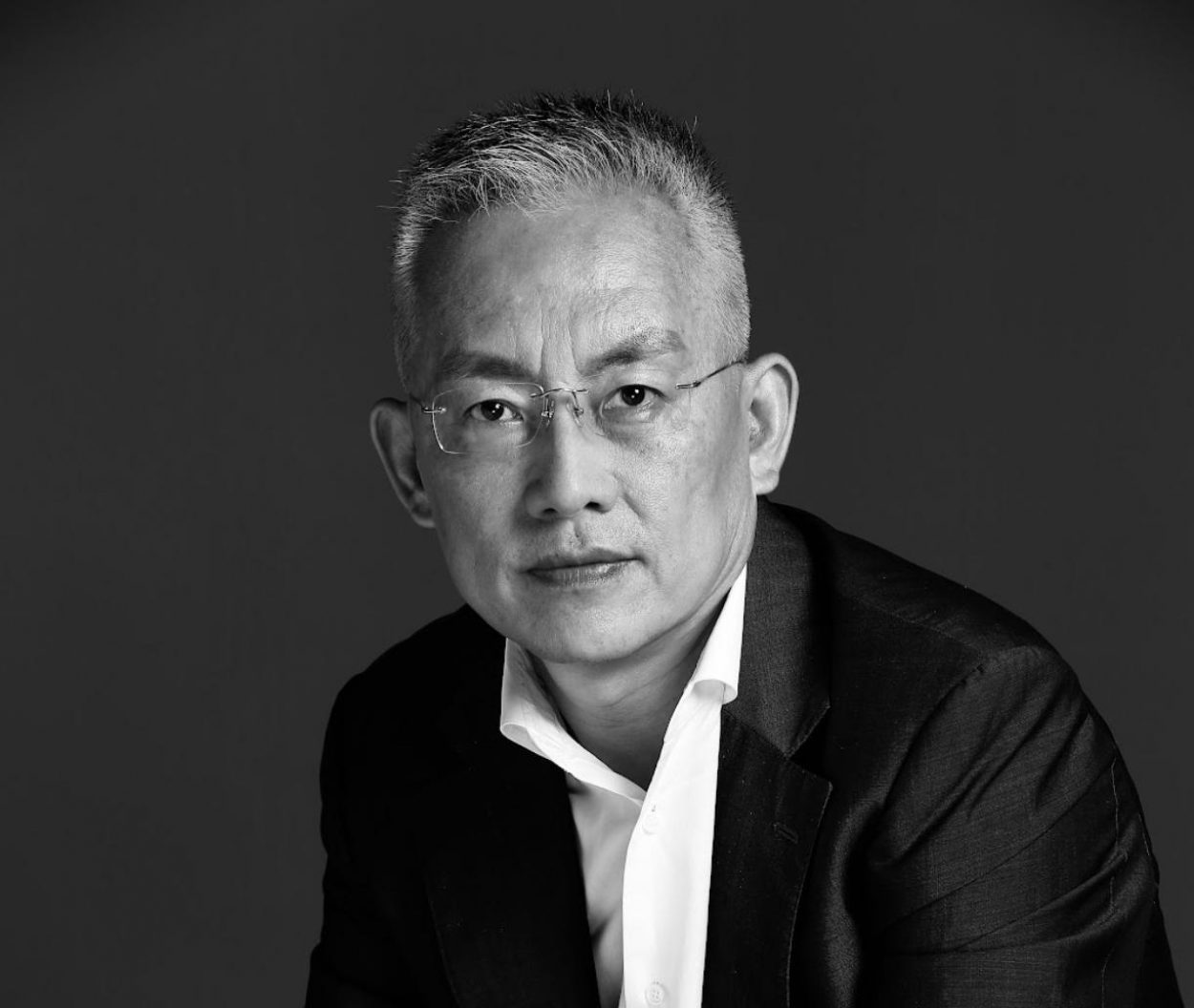 Black and white portrait of MIT alum Qian Wang wearing glasses and a black and white suit