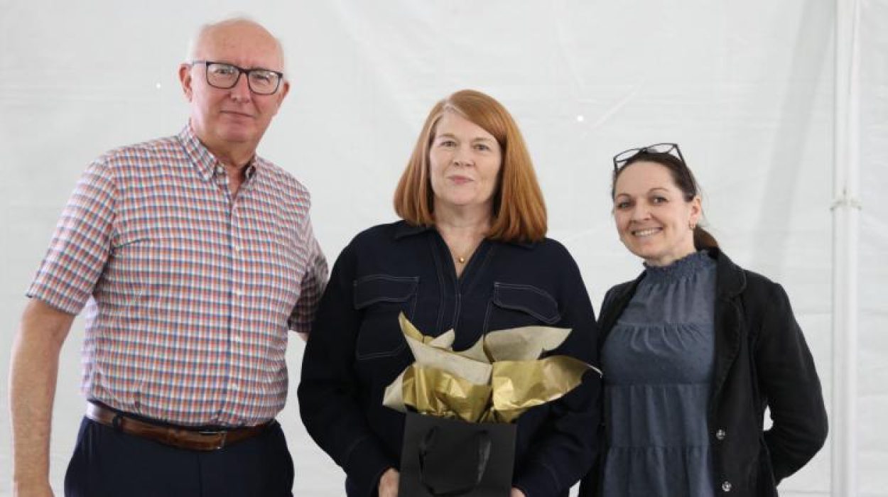 three people pose for camera, awardee in the middle holds flowers